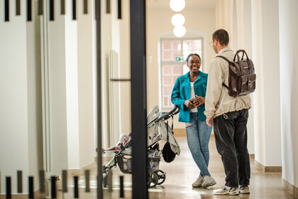 Zwei Personen mit Kinderwagen in einem Flur der Universität
