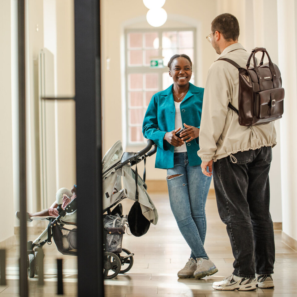 Zwei Personen mit Kinderwagen in einem Flur der Universität