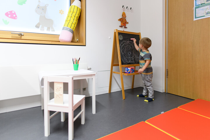 Ein Junge im Kindergartenalter, der mit Kreide auf eine Tafel malt.