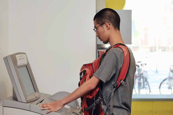 Ein Student steht an einem elektronischen SB-Terminal der Universität Mannheim. Er trägt einen roten Rucksack auf seinem Bauch.