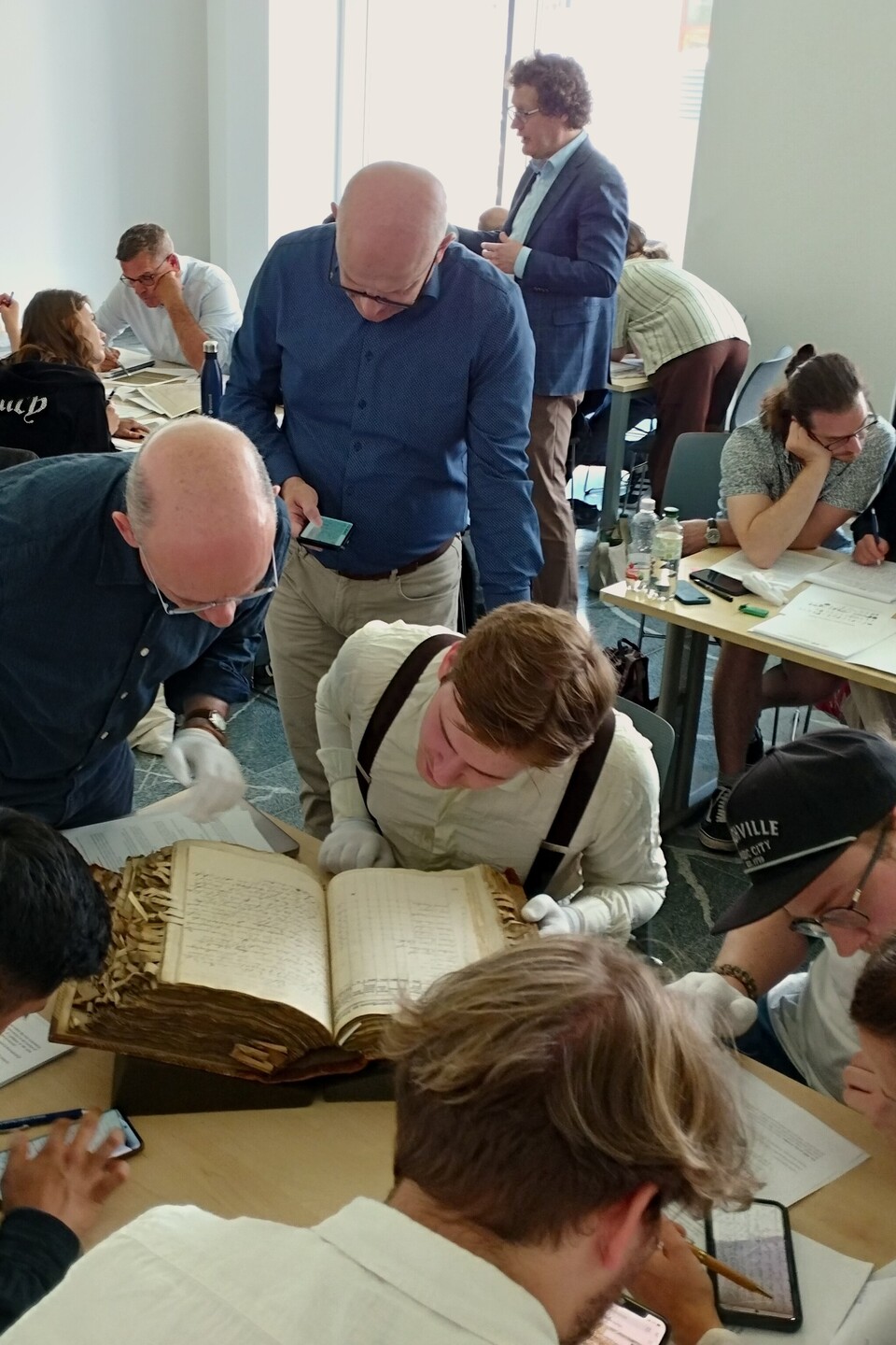 Die Teilnehmenden der Summer School diskutieren in Kleingruppen lebhaft und studiert gemeinsam historische Handschriften in einem Klassenzimmer.