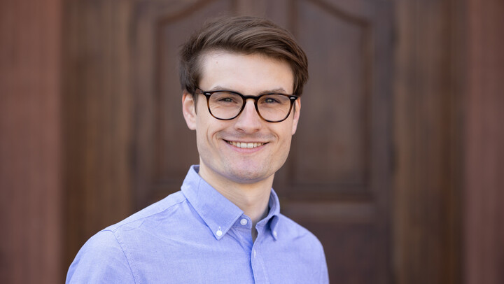 Ulrich Roschitsch. He is wearing a blue shirt and is standing in front of a brown door.
