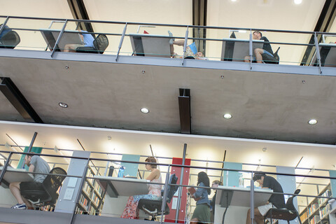 Studierende sitzen auf verschiedenen Etagen der Bibliothek an Arbeitsplätzen.