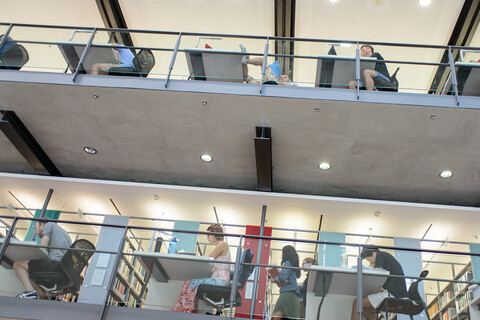 Studierende sitzen auf verschiedenen Etagen der Bibliothek an Arbeitsplätzen.