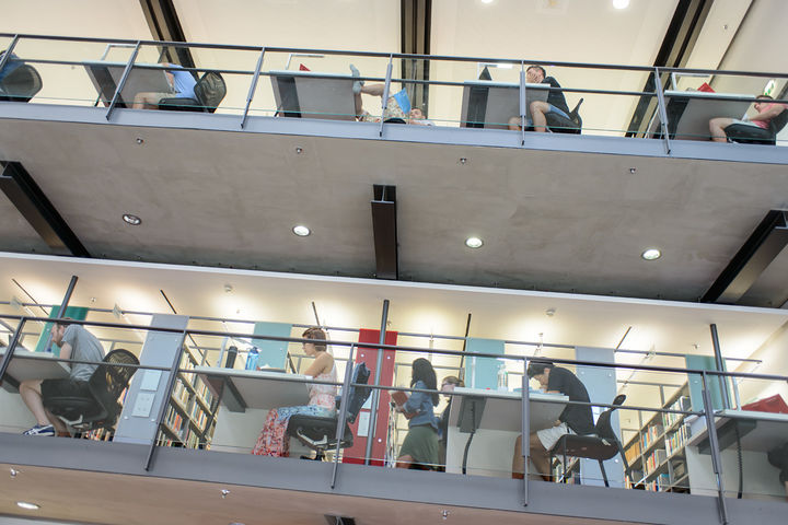 Studierende sitzen auf verschiedenen Etagen der Bibliothek an Arbeitsplätzen.