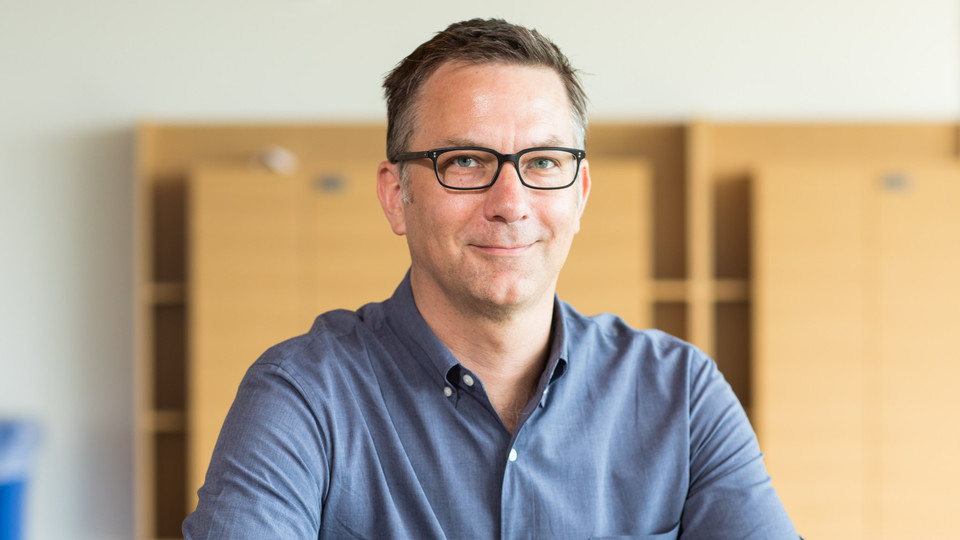 Portrait von Matthias Doepke. Er trägt ein blau-graues, langärmeliges Hemd.