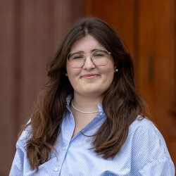 Michelle trägt eine blau-weiß gestreifte Bluse und lächelt in die Kamera.