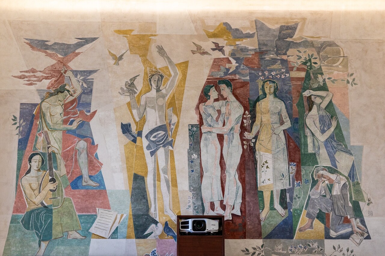 Bunte Wandmalerei mit acht Personen in verschiedenen Posen. Unten in der Mitte ist ein Beamer in die Wand eingebaut.