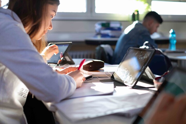 Eine Studentin mit weißem Kapuzenpullover sitzt vor einem Tablet
