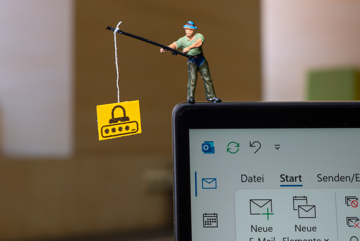 Eine Miniaturfigur eines Anglers steht auf einem Laptop-Bildschirm und angelt ein Schild mit einem Passwort-Symbol.