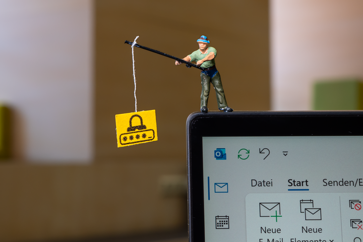 Eine Miniaturfigur eines Anglers steht auf einem Laptop-Bildschirm und angelt ein Schild mit einem Passwort-Symbol.