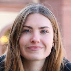 Milena Gropp hat blaue Augen, dunkelblonde Haare und lächelt. Sie trägt silberne Ohrringe und eine dunkelblaue/schwarze Jacke.