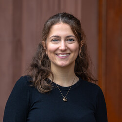 Annika lächelt freundlich in die Kamera. Sie hat lockige, braune Haare und trägt ein schwares Oberteil.