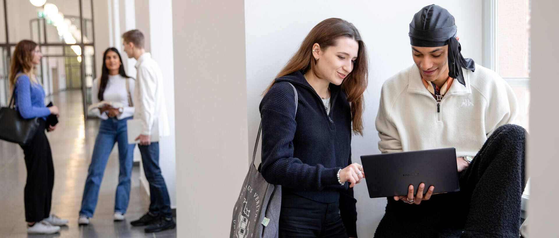 Students stand and sit in groups in the corridor of the Ehrenhof West.