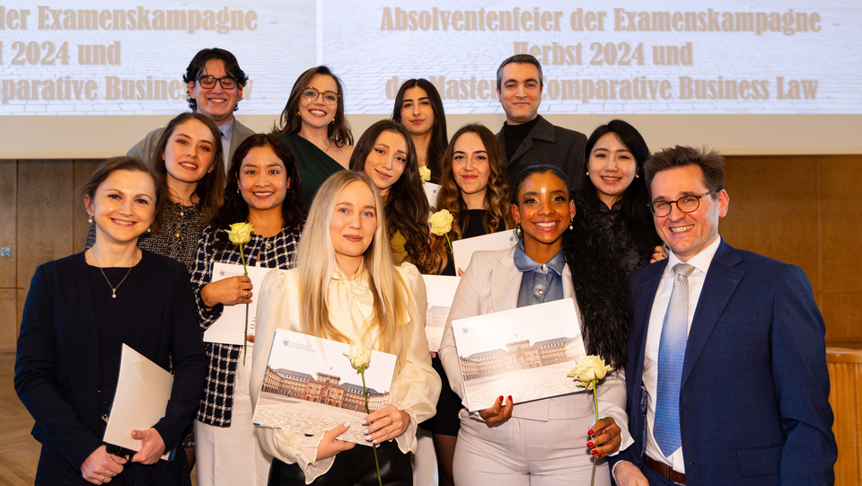 Gruppe von Absolventinnen und Absolventen sowie von Frau Dr. Fischinger-Corbo und Herrn Prof. Dr. Kainer in der Aula des Schlosses. Sie lächeln alle.