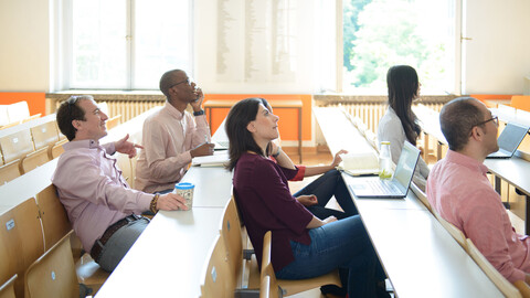 Fünf Studierende sitzen in einem Vorlesungsraum und hören sich einen Vortrag an.