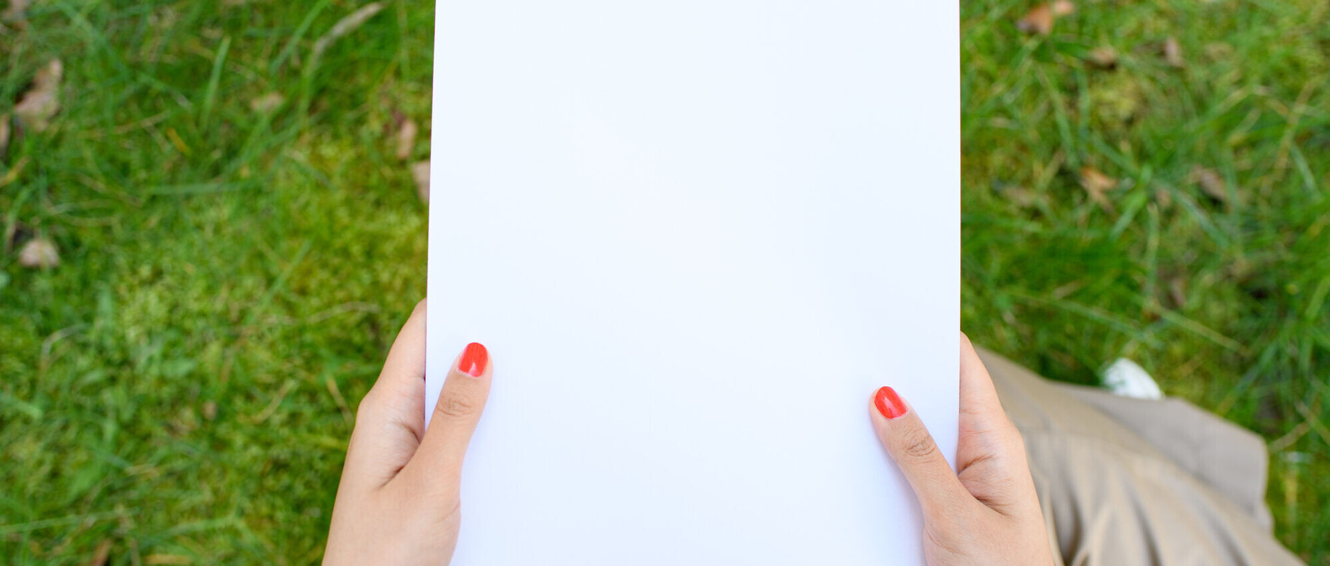 Eine Person mit roten Fingernägeln hält ein leeres Blatt Papier in den Händen