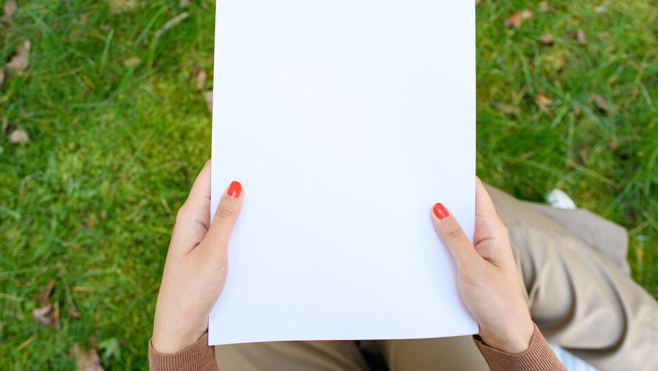 Eine Person mit roten Fingernägeln hält ein leeres Blatt Papier in den Händen