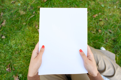 Eine Person mit roten Fingernägeln hält ein leeres Blatt Papier in den Händen