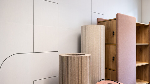 Auf dem Foto sind Details einer weißen schallhemmenden Fließwand zu sehen. Davor stehen stoffbezogene Säulen. Man sieht die Hälfte eines Raumteilers.