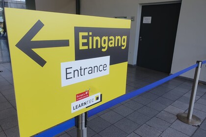 Hinweisschild in gelb und schwarz, das mit einem Pfeil den Eingang ausweißt zur LEARNTEC 2025