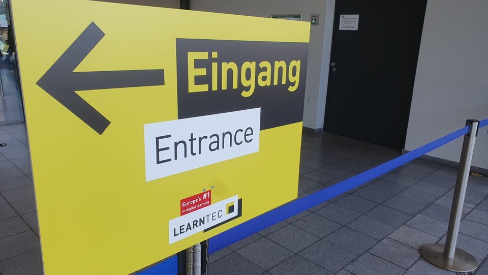 Hinweisschild in gelb und schwarz, das mit einem Pfeil den Eingang ausweißt zur LEARNTEC 2025