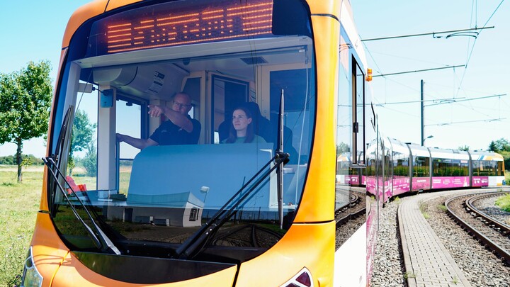 Blick von außen in den Führerstand der Straßenbahn, in der ein Mitarbeiter der rnv Marleen Quurk etwas erklärt.