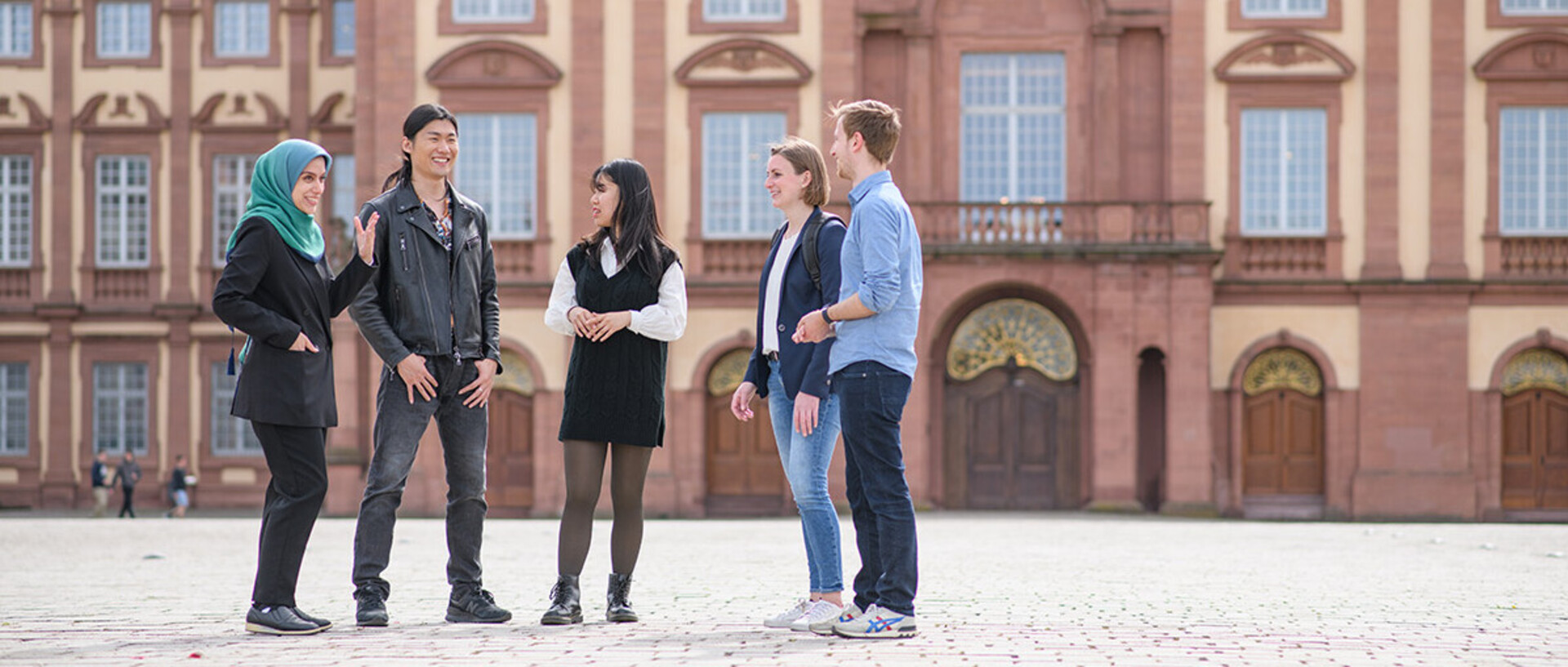 A group of doctoral students are laughing and standing on the Ehrenhof in front of the castle.