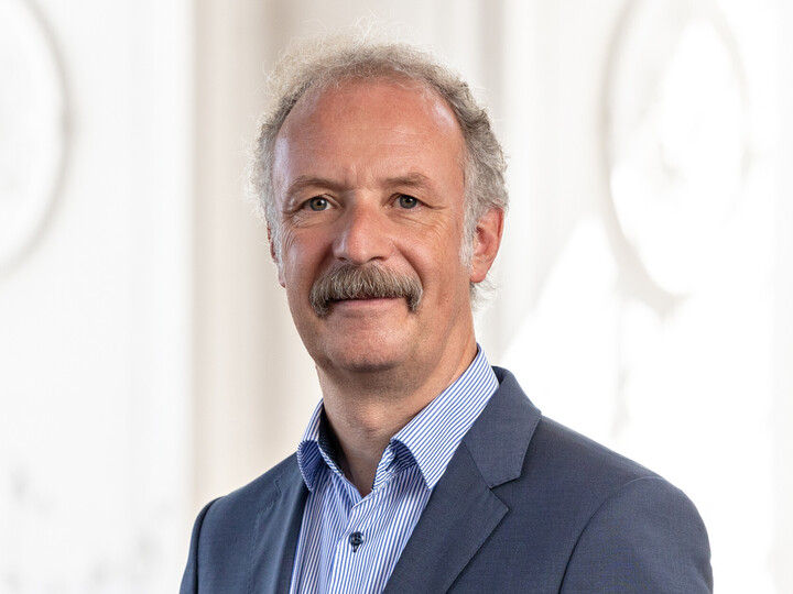 Prof. Dr. Moritz Fleischmann hat graue Haare und einen Schnauzer. Er trägt ein dunkles Jackett und ein gestreiftes Hemd.