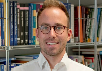 Andreas Bayerl. He is wearing a white shirt and is standing in front of a book shelf.