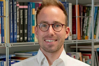 Andreas Bayerl. He is wearing a white shirt and is standing in front of a book shelf.