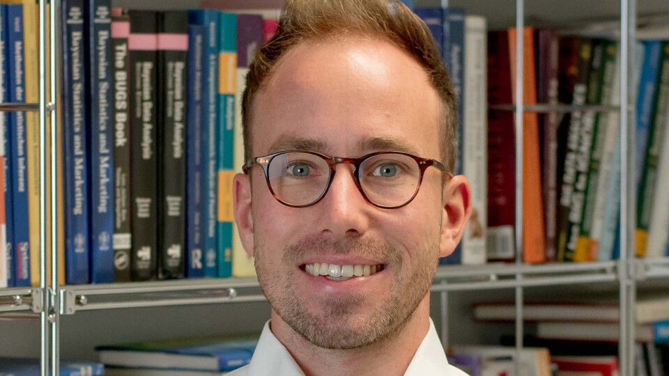 Andreas Bayerl. He is wearing a white shirt and is standing in front of a book shelf.