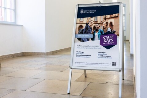 Aufsteller in Schloss informiert über 'Staff Days' der Universität Mannheim, die am 14. und 15. Mai 2024 stattfinden.Drei fröhliche Personen abgebildet. Angeboten werden Workshops, Führungen, soziale Events usw. QR-Code für mehr Infos.