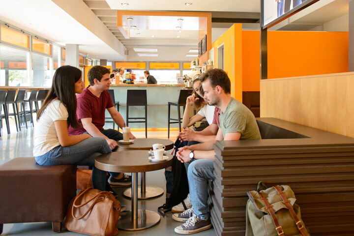 Eine Gruppe von Studierenden sitzt um einen Café-Tisch in der Mensa.