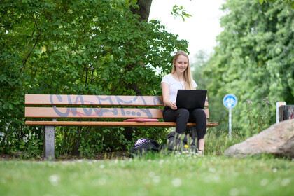 Studentin mit Laptop auf einer Parkbank