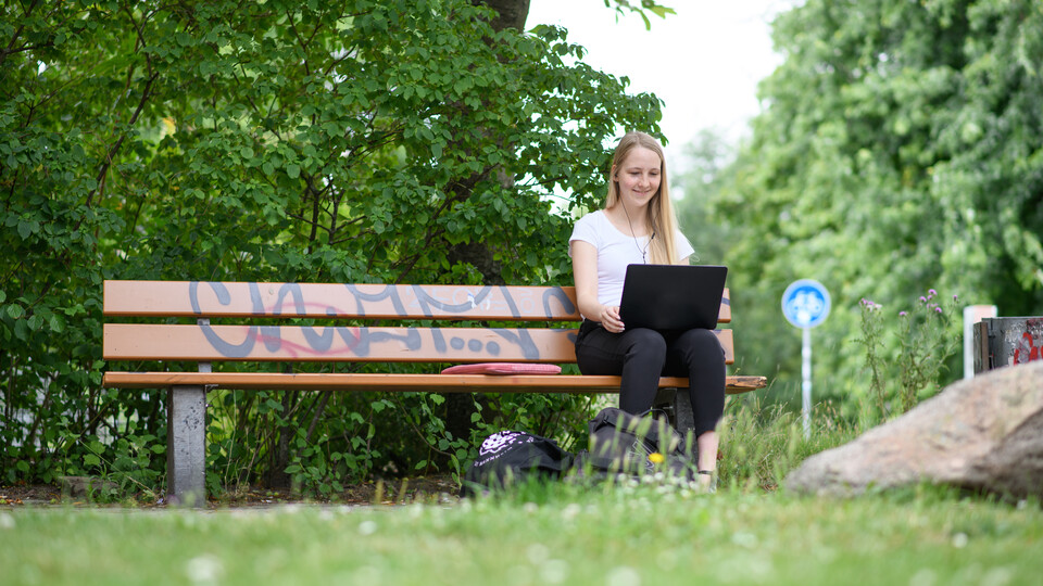 Studentin mit Laptop auf einer Parkbank