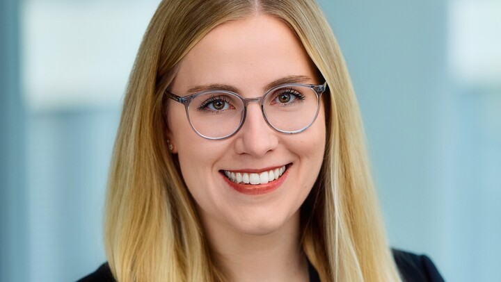 Portraitfoto von Jette Völker. Sie trägt ein schwarzes Obterteil und eine Brille und lächelt in die Kamera.
