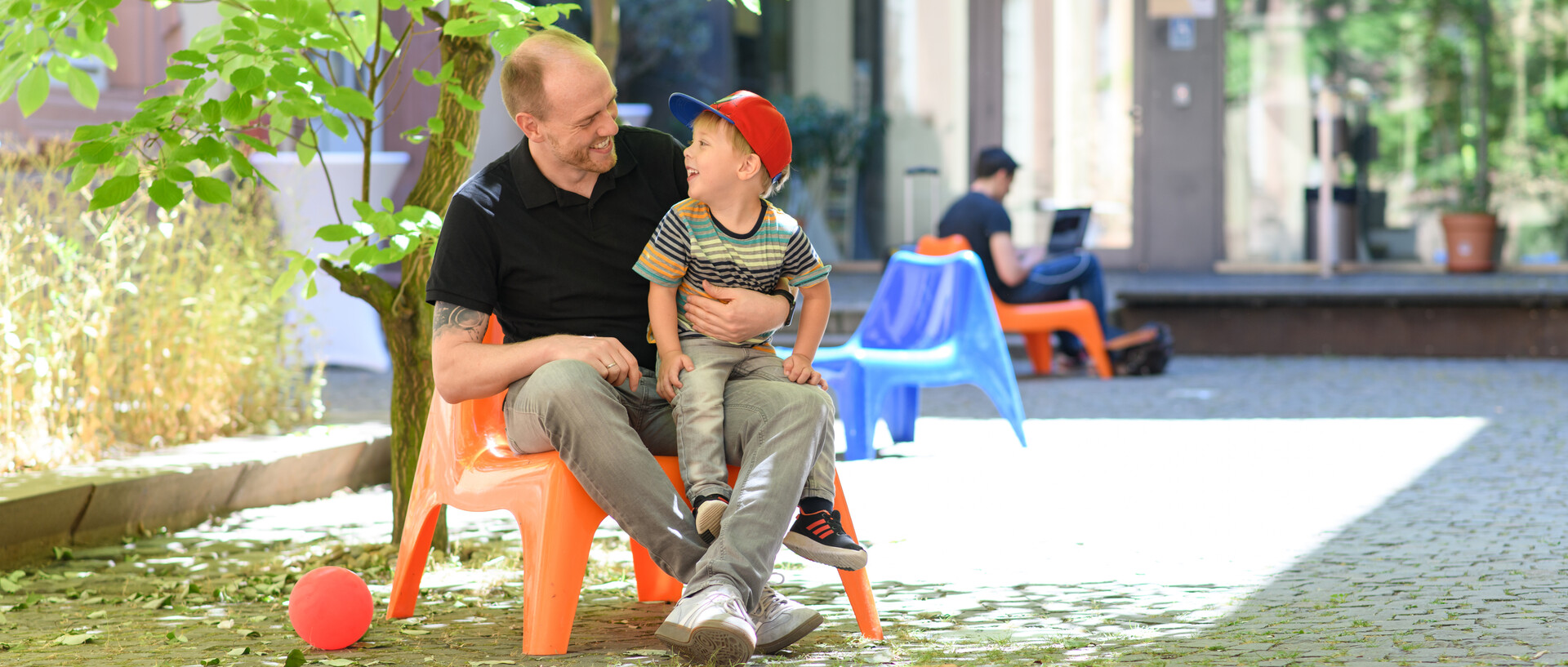 Vater und Sohn sitzen auf dem Gelände der Universität Mannheim und lächeln sich an.