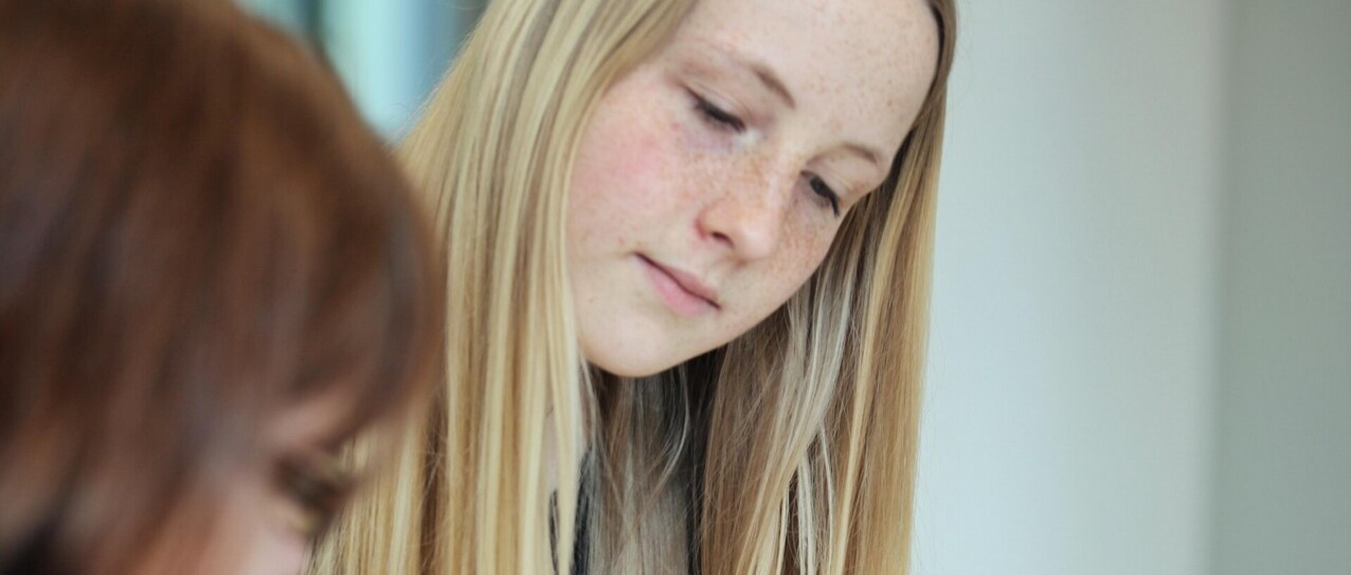 Eine Studentin mit langen blonden Haaren betrachtet etwas vor sich auf dem Tisch.