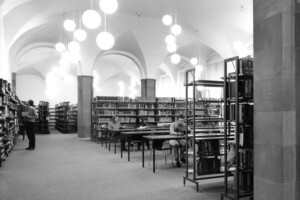 schwarz-weiß Aufnahme des damaligen Lesesaals im Ostflügel der Universität Mannheim. Studierende sitzen zwischen den Bücherregalen und lernen.