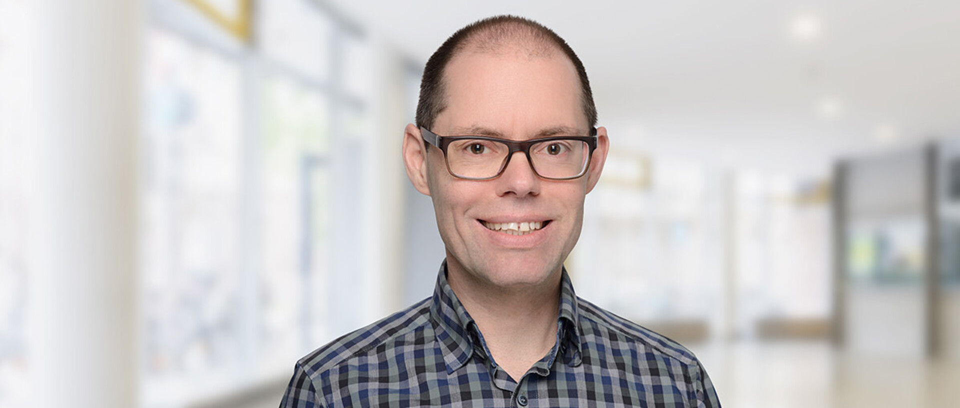 Portrait von Martin Peitz. Er trägt ein karriertes dunkelblau-schwarzes Hemd und lächelt.
