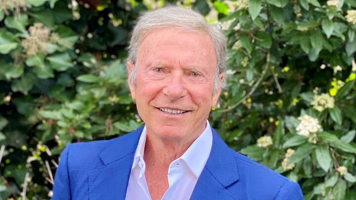 Eine lächelnde Person trägt ein weißes Hemd sowie einen blauen Blazer und steht vor einer Hecke. Die Person heißt Hans-Peter Wild.