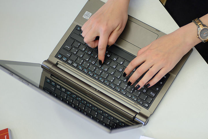 Zwei Hände einer Frau tippen auf der Tastatur eines Laptops.