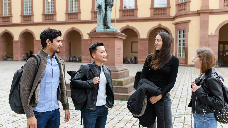 Vier Studierende unterhalten sich im Ehrenhof des Schlosses