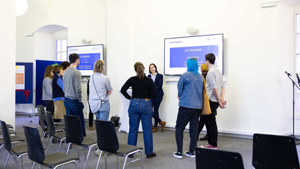 Teilnehmende des Tags der Lehre stehen diskutierend im Kreis. An der Wand ein Monitor mit der Aufschrift ZLL-Werkstatt.