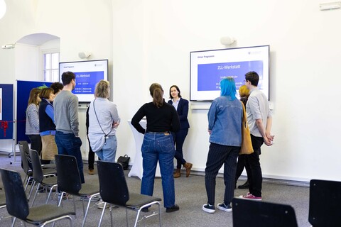 Teilnehmende des Tags der Lehre stehen diskutierend im Kreis. An der Wand ein Monitor mit der Aufschrift ZLL-Werkstatt.