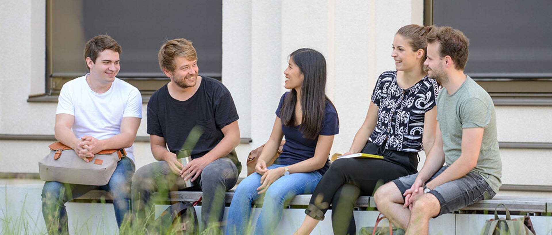 Eine Gruppe von Studierenden sitzt in entspannter Atmosphäre draußen auf einer langen Bank