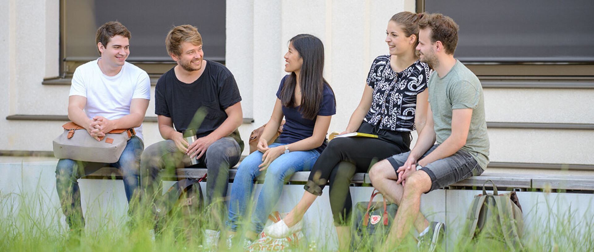 Eine Gruppe von Studierenden sitzt in entspannter Atmosphäre draußen auf einer langen Bank