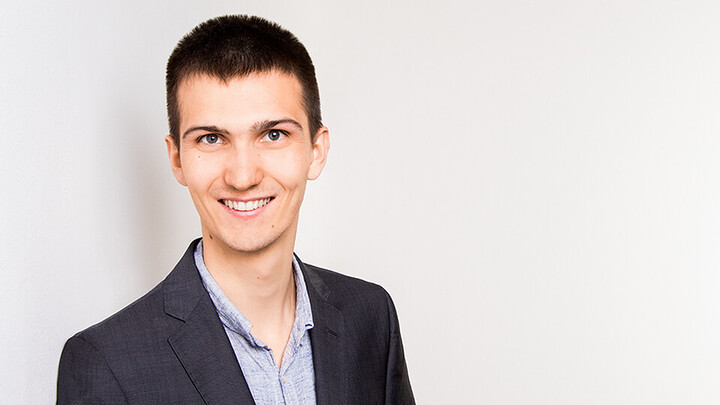 Lukas Isermann. He is wearing a black suit in front of a white background.