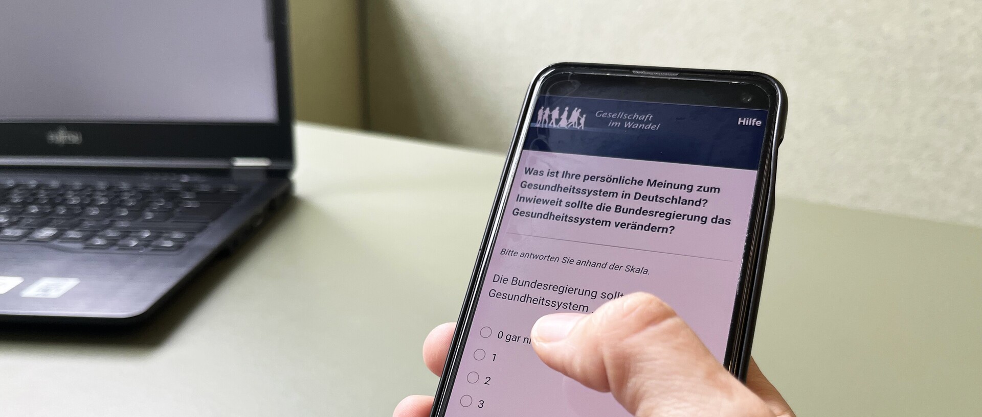 Person answering the GIP questionnaire on the smartphone. The screen reads: “What is your personal opinion of the healthcare system in Germany?”